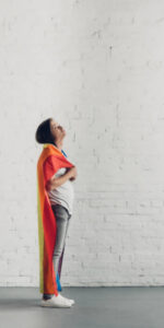 person with rainbow flag around their shoulders looking up